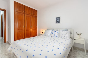 Une chambre à coucher comprenant un lit, une armoire en bois, une table de chevet, une lampe et un tableau accroché au mur.