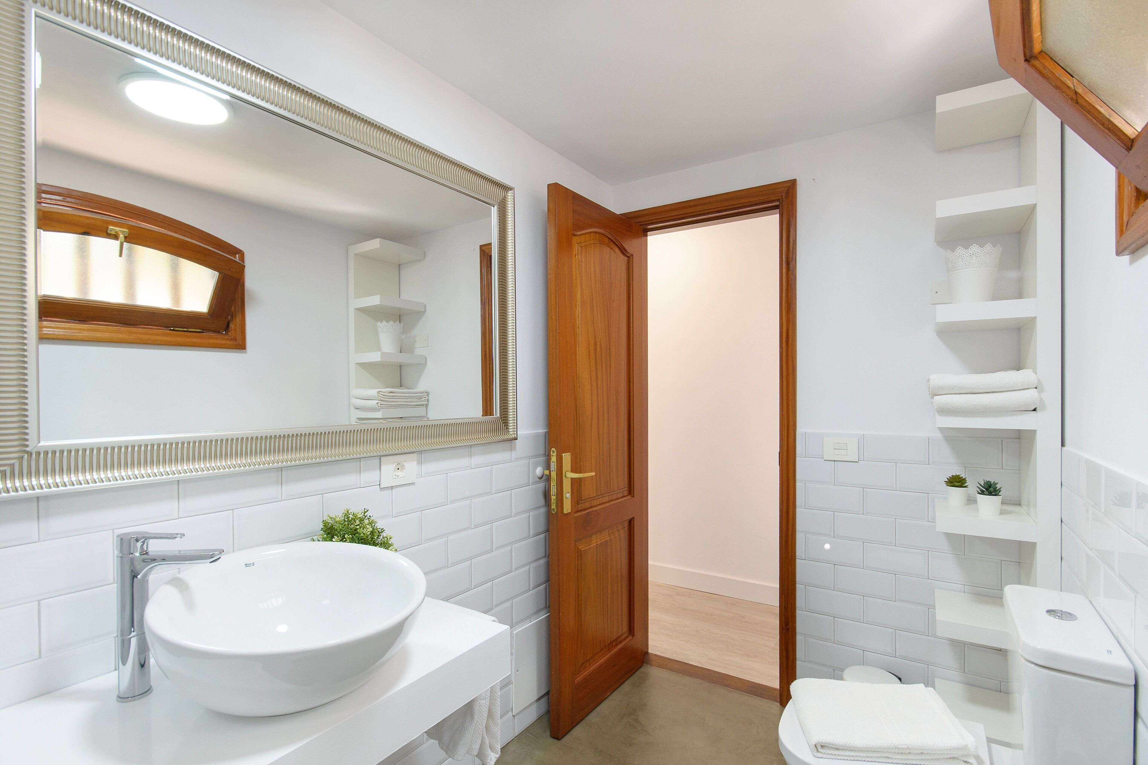 Un baño con lavamanos blanco, espejo y puerta de madera.