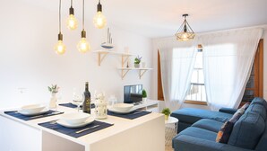 Una cocina moderna con una isla central, iluminación colgante y una zona de comedor con sofá y cortinas.