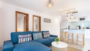 Una sala de estar moderna con un sofá azul, una mesita redonda y una cocina con taburetes y un microondas.