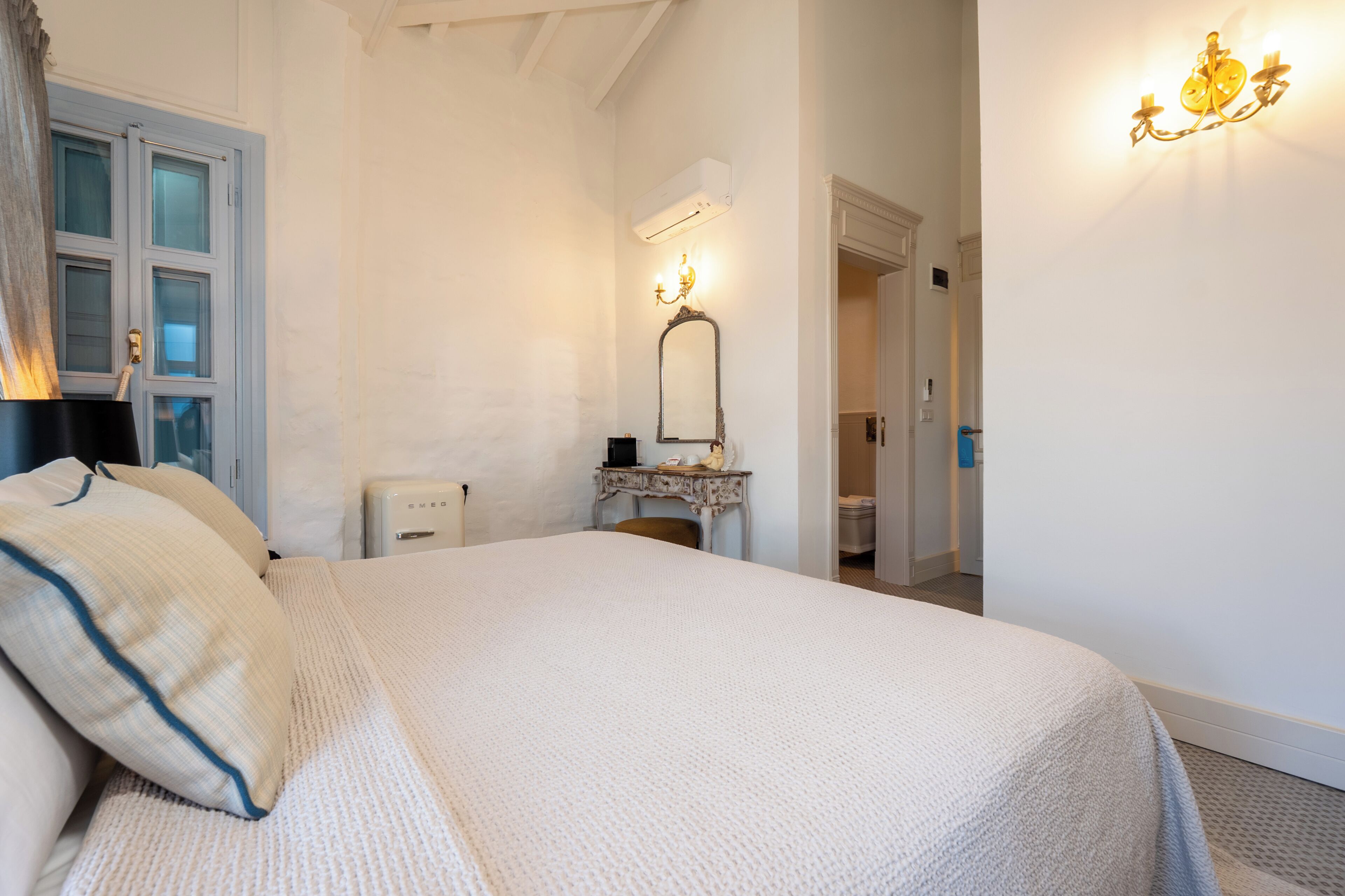 Une chambre à coucher avec un grand lit, une table de chevet, un miroir et un luminaire fixé au mur.