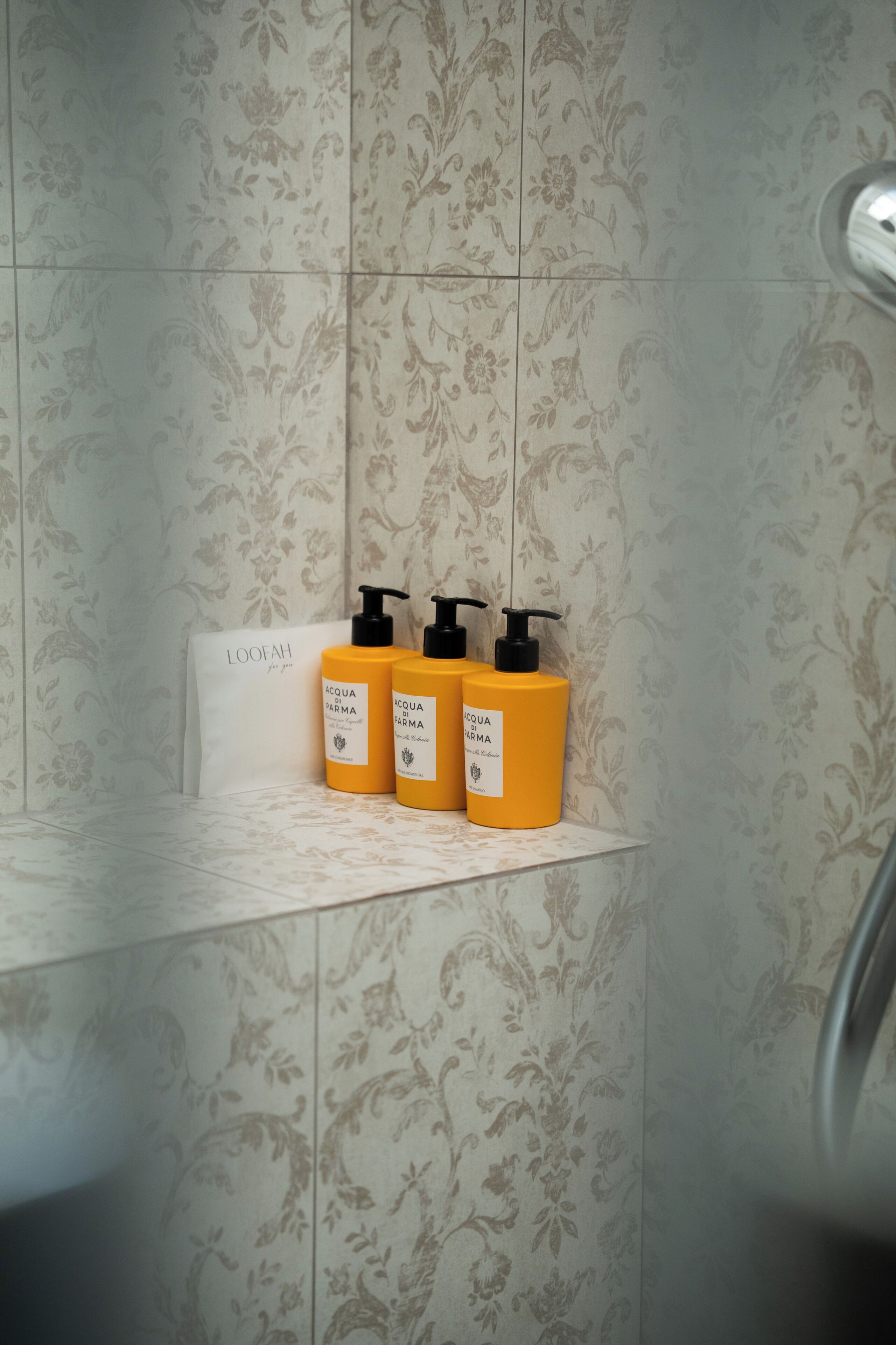 A bathroom with floral patterned tiles, a white towel, and three yellow bottles of Aquafarma shampoo.