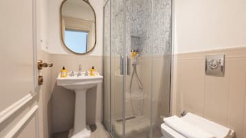 A bathroom with a pedestal sink, a glass-enclosed shower, a toilet, and a mirror with an ornate frame.