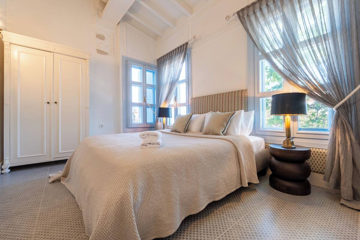 Ein Schlafzimmer mit einem großen Bett, einem Kleiderschrank, einem Fenster mit Vorhängen und einer Nachttischlampe.