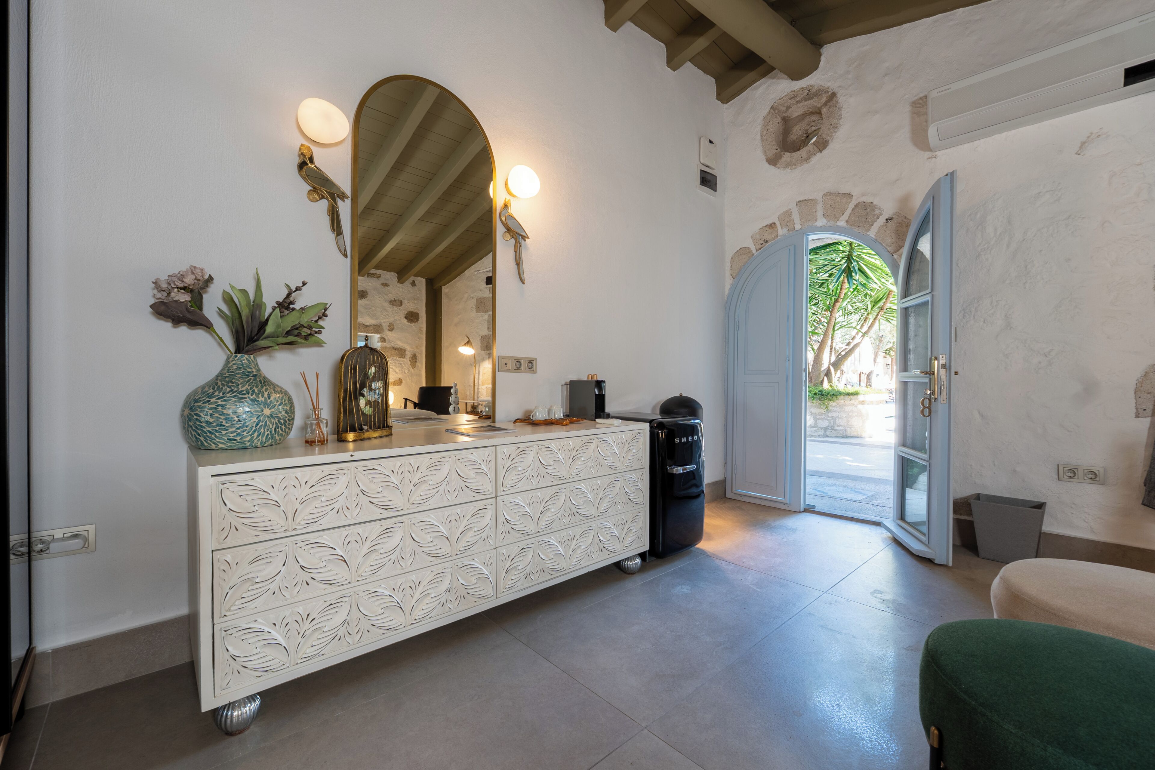 A room with a white cabinet, a mirror, a vase, and a door leading outside.