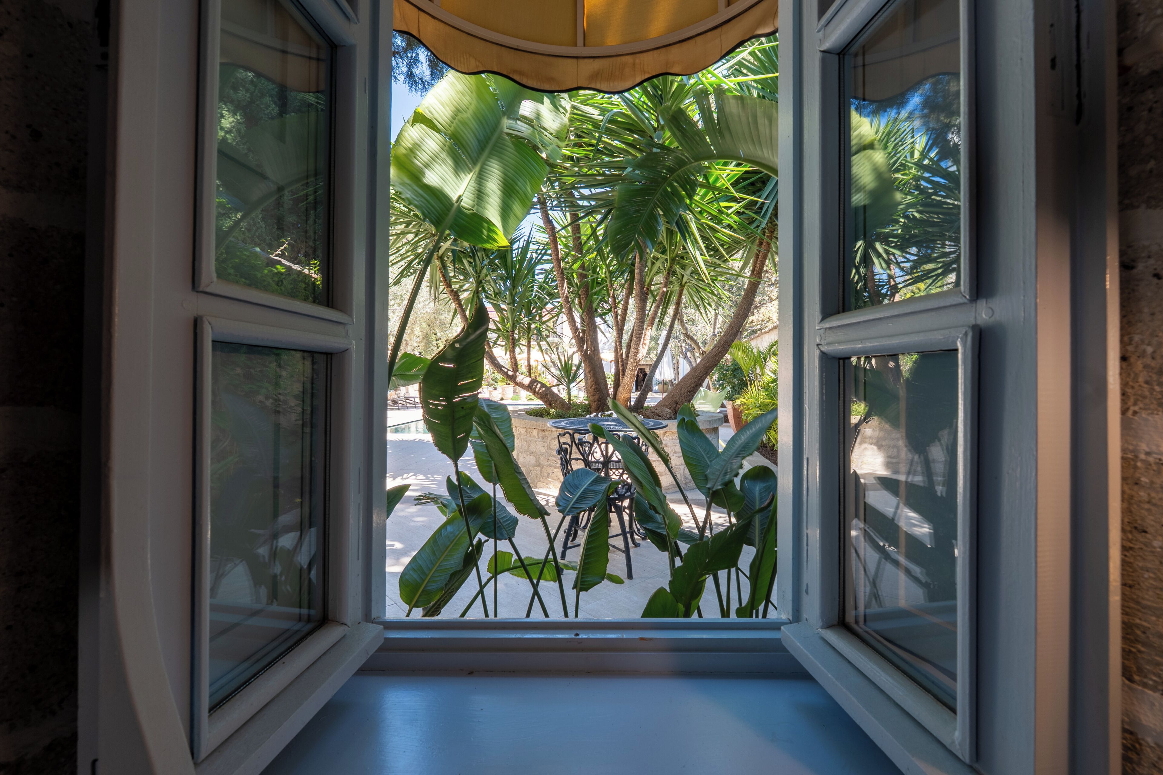 A window with a view of outdoor seating and palm trees.