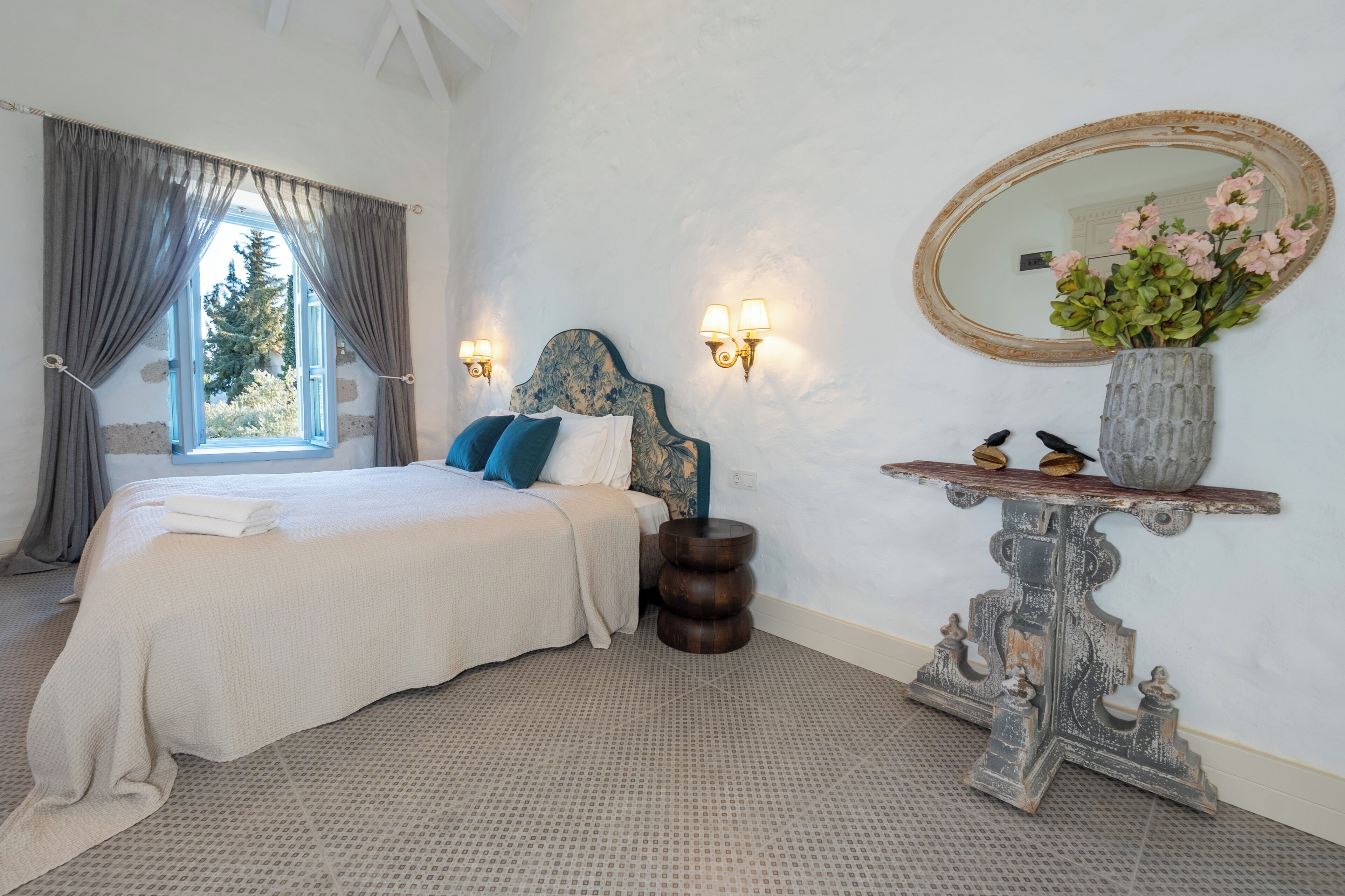 A bedroom with a bed, a nightstand, a mirror, and a window with curtains.