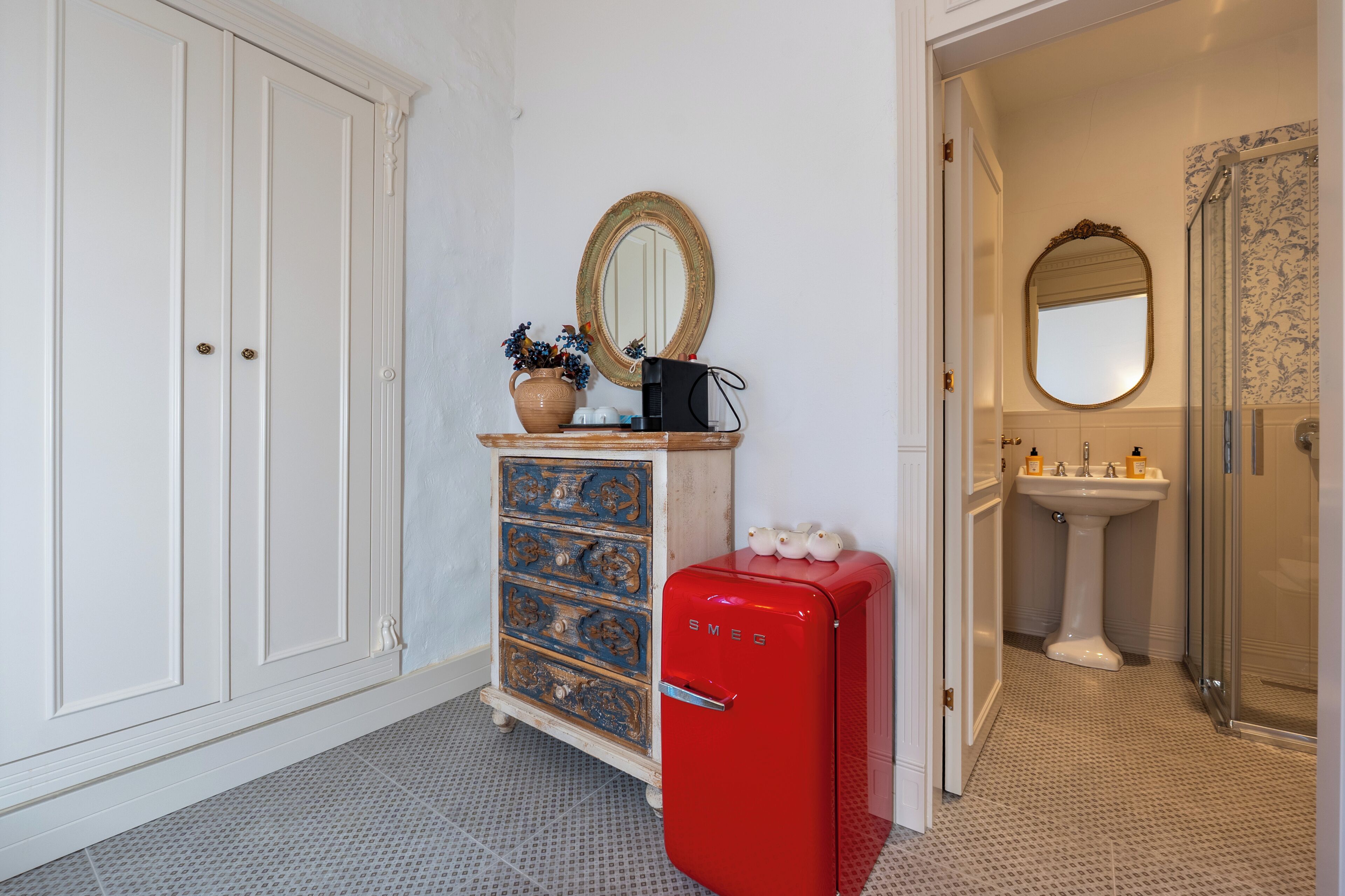 A bathroom with a shower, a sink, a mirror, a vintage refrigerator, and a cabinet with drawers.