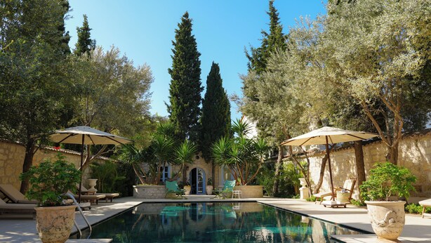 A pool area with lounge chairs and umbrellas, surrounded by trees and a stone building. - Tas Otel (Cesme)