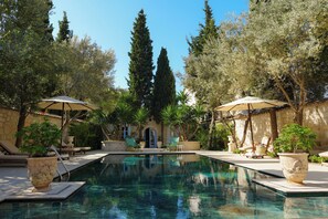 A pool area with lounge chairs and umbrellas, surrounded by trees and a stone building. - Tas Otel (Cesme)
