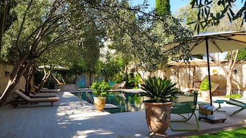 A poolside area with lounge chairs, potted plants, and a pergola providing shade.