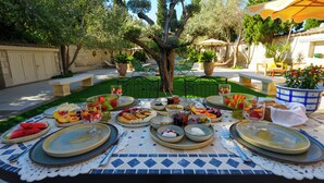 An outdoor dining area with a table set for a meal, surrounded by greenery and trees. - Tas Otel (Cesme)