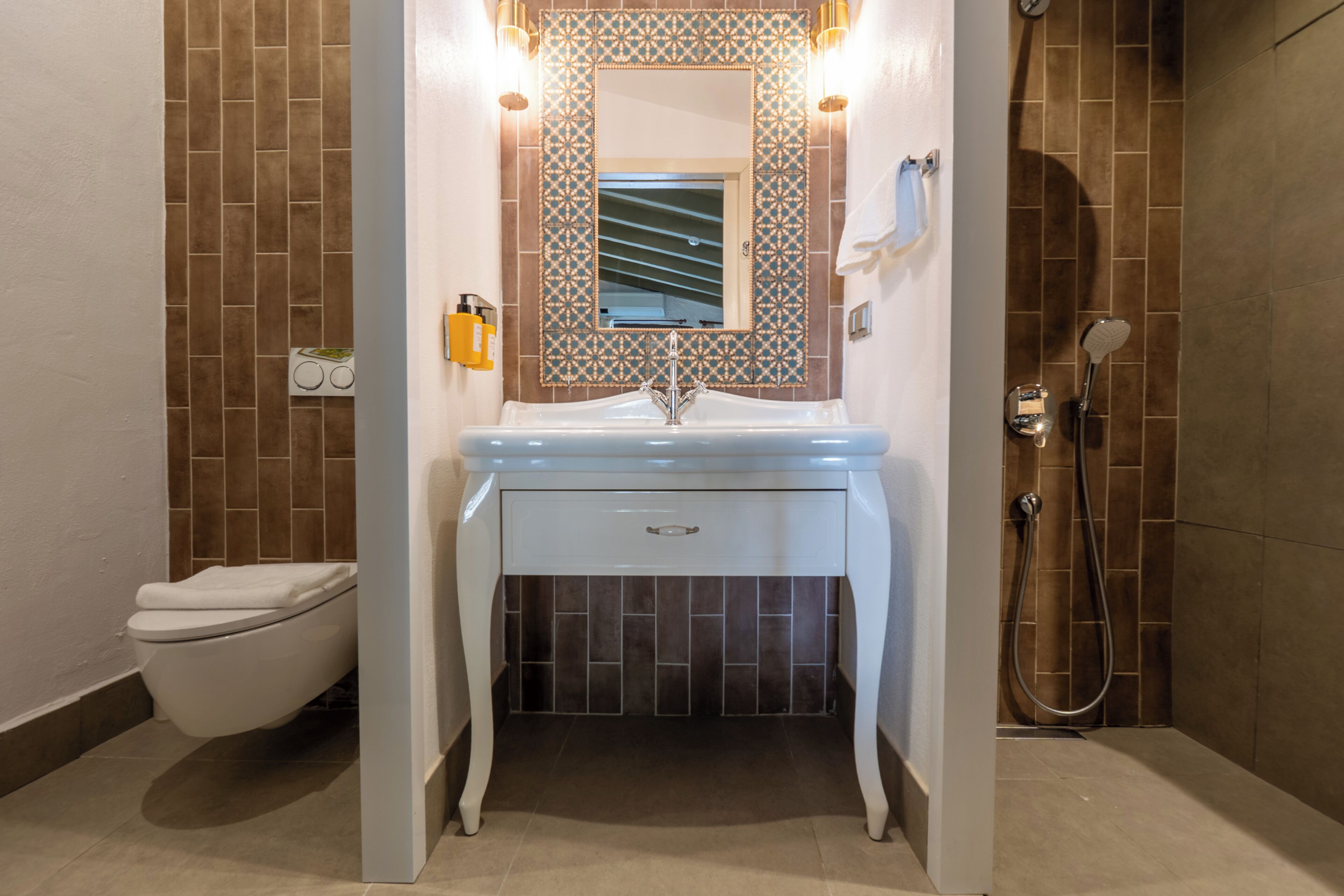 Une salle de bain avec un lavabo blanc, un miroir doté d’un cadre décoratif, une douche et des toilettes.