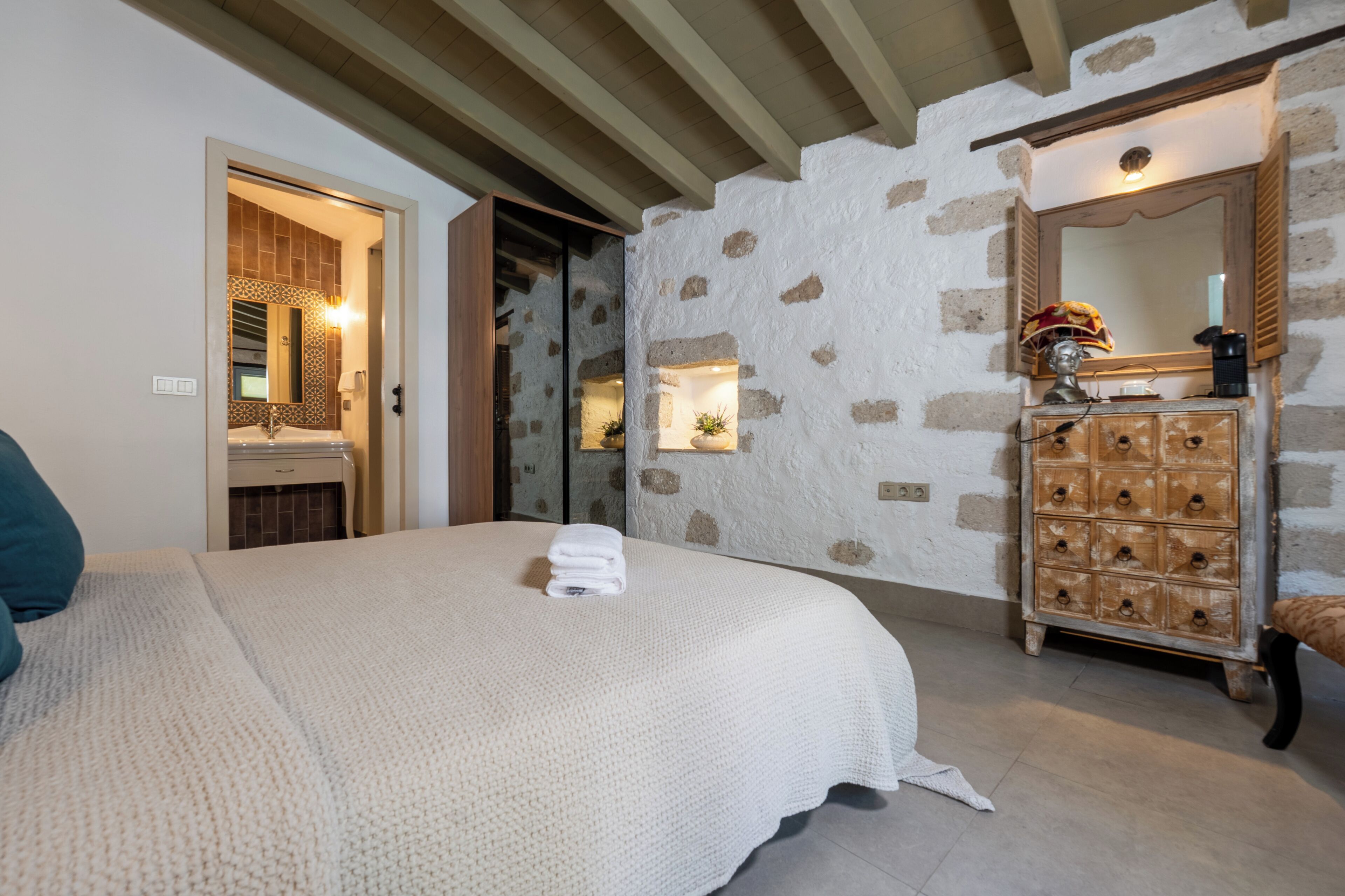 A bedroom with a bed, a dresser, a mirror, and a stone wall.