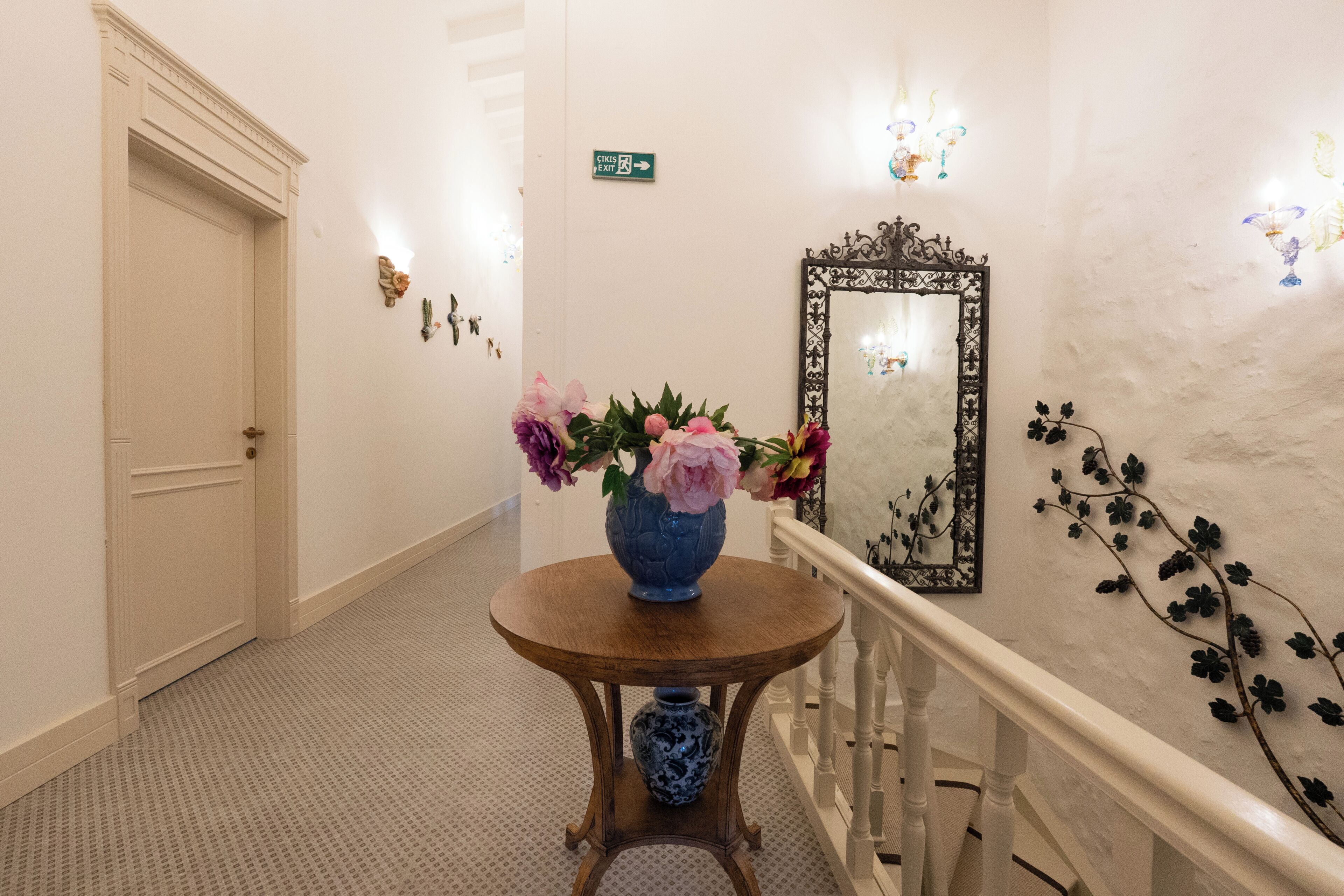 Un couloir avec une table ronde en bois, un vase de fleurs, un miroir et un panneau fixé au mur.