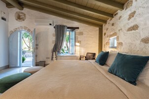 A bedroom with a large bed, a window with curtains, a chair, and a lamp.