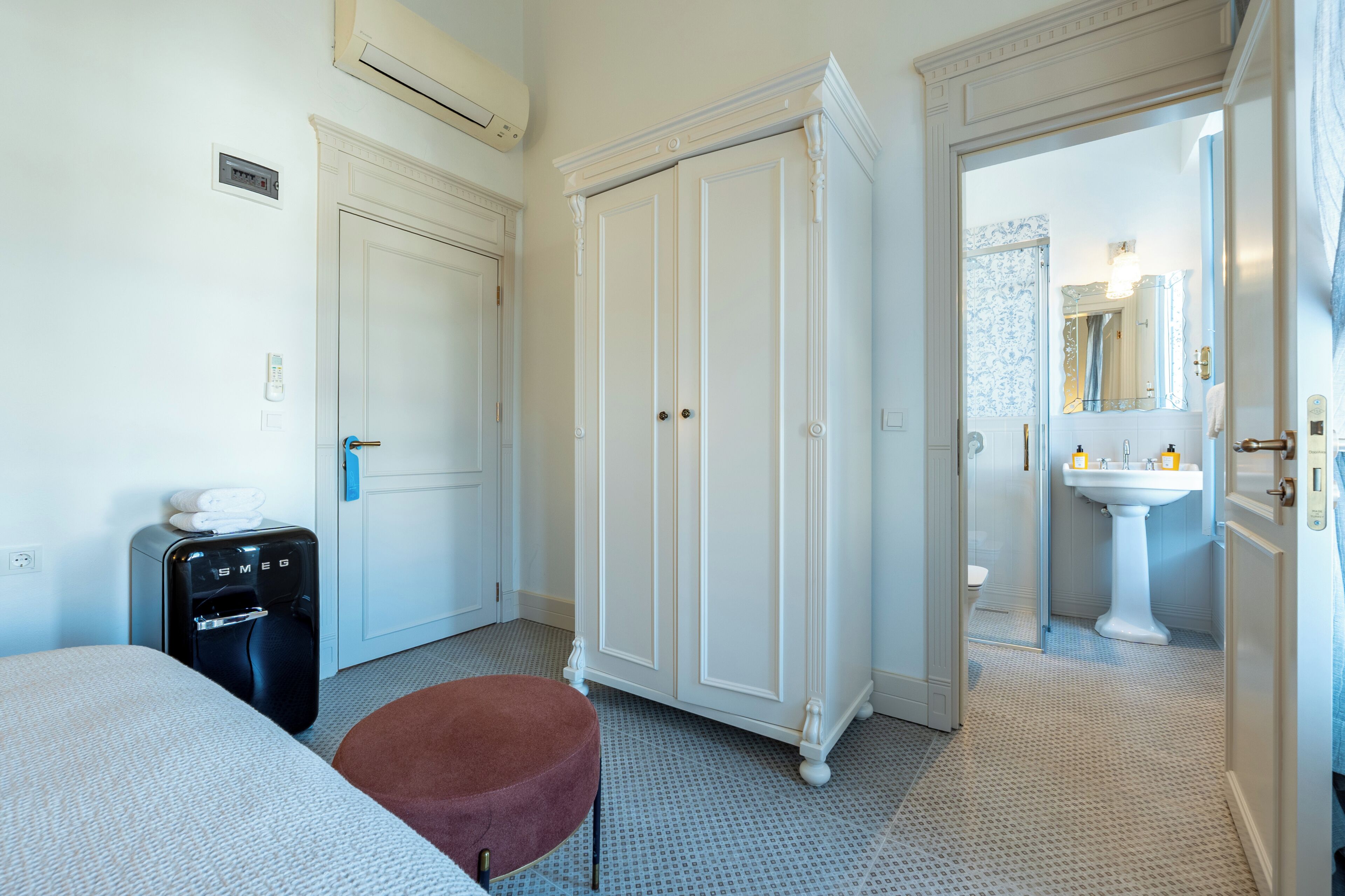 Une chambre d’hôtel équipée d’un lit, d’un minibar, d’une armoire et d’une salle de bain visible à travers une porte ouverte.