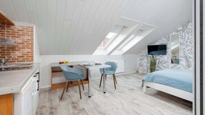 Een compacte, moderne slaapkamer met een schuine kap, een bed, een bureau met twee stoelen, en een kleine kitchenette.
