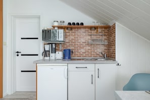 A compact kitchen with a dishwasher, a coffee maker, a toaster, and a kettle on the countertop.