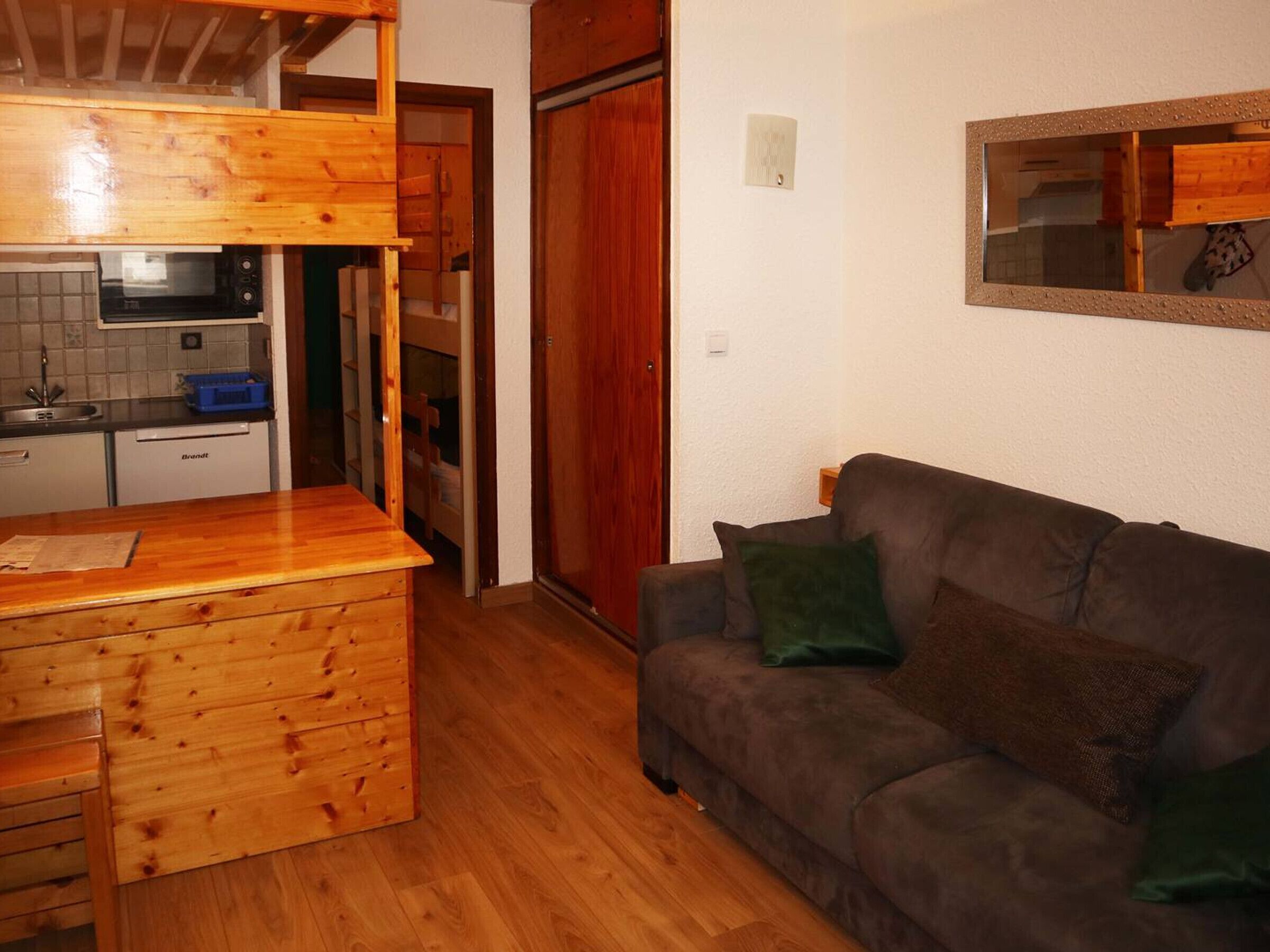 A compact living space with a kitchenette, wooden furniture, and a sofa with cushions.