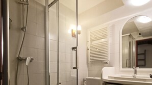 A bathroom with a glass shower enclosure, a toilet with a blue seat, a sink with a mirror, and a towel rack.