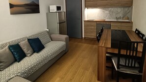 A compact living space with a sofa, a dining table with chairs, a kitchen area with wooden cabinets, and a refrigerator.