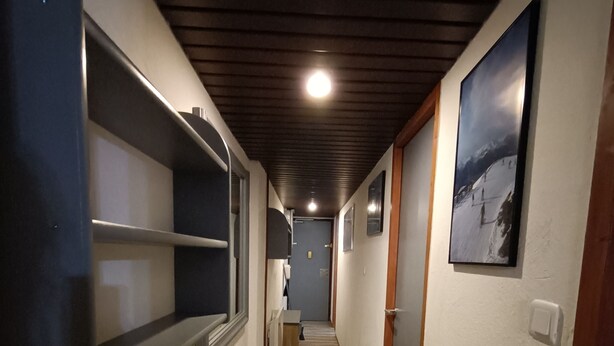 A narrow hallway with wooden beams on the ceiling, a light fixture, and a door at the end.