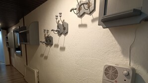 A hallway with a wooden bench, a wall-mounted heater, and a wall-mounted fan.
