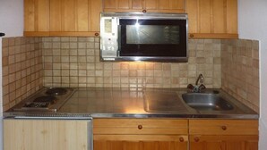 A kitchen with wooden cabinets, a stainless steel sink, a microwave, and a gas stove. - Charming studio in Les Orres for 4, ski-in/ski-out, balcony (Les Orres)