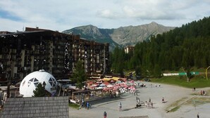 A building with multiple floors and balconies, a dome-shaped structure, and a mountainous backdrop. - Charming studio in Les Orres for 4, ski-in/ski-out, balcony (Les Orres)