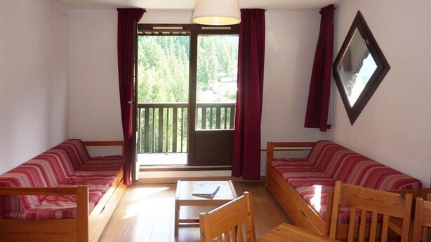A room with two wooden sofas, a wooden table, and a chair. There is a window with curtains, a lamp, and a mirror on the wall. - Cozy studio, ski-in/ski-out, central location, sleeps 6, south-facing balcony (Les Orres)