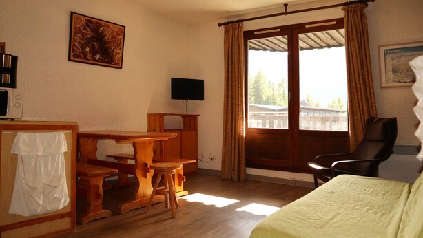 A room with a bed, a desk with a chair, a television, and a window with curtains.