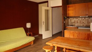 A compact room with a bed, a small table, a stool, and a kitchenette.