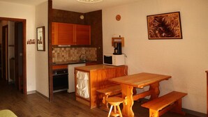 A compact kitchen with wooden cabinets, a microwave, and a coffee maker. There is a wooden dining table with benches.