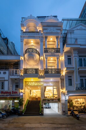 Un hotel con una entrada imponente, una escalera que conduce al vestíbulo y un letrero que dice 'Wisteria Hotel'.