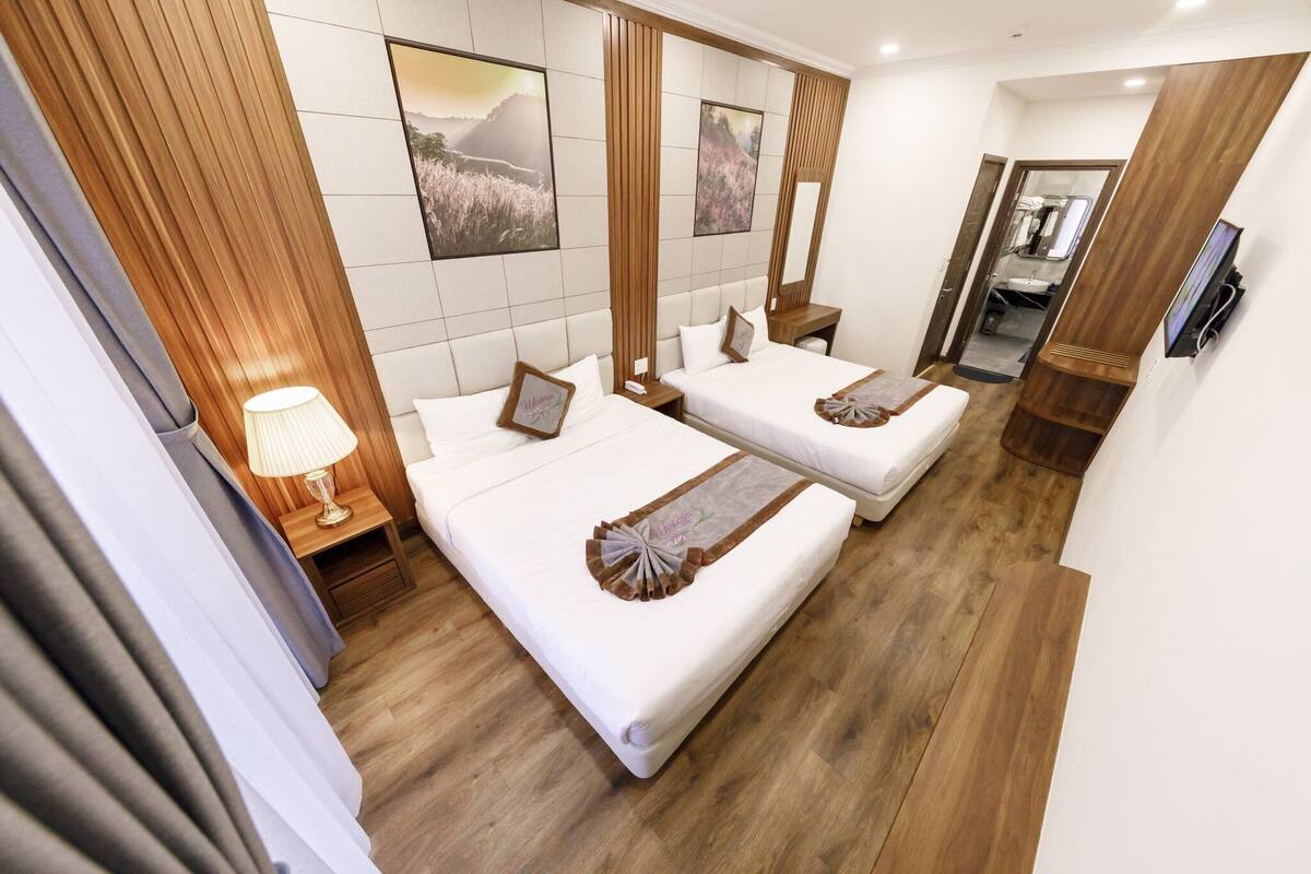 Une chambre d’hôtel avec deux lits, un plancher en bois, un grand miroir et des œuvres d’art accrochées aux murs.