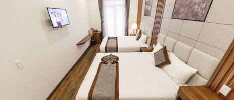 A hotel room with two beds, a TV, a window with curtains, and a painting on the wall.