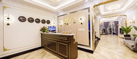 A hotel reception area with a marble floor, a reception desk, and a chandelier.