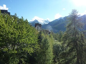 A mountainous landscape with dense forest and a building with multiple floors, likely a hotel or resort, in the background. - Lovely 2-room apt, renovated, south balcony, Les Orres (Les Orres)