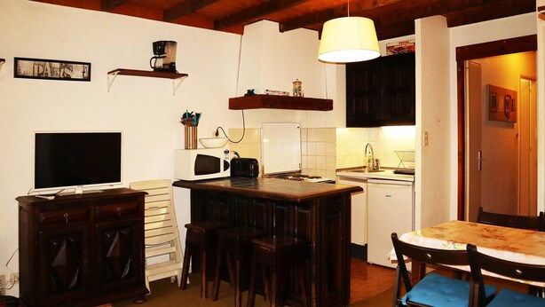 A compact kitchen with a wooden table and bar stools, a microwave, a toaster, and a hanging lamp. - Family studio 4 pers, ski-in/ski-out, near center (Les Orres)