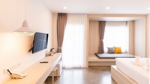 A modern hotel room with a wooden desk, a flat-screen TV, a bed with white bedding, and a seating area with cushions. - Nappiness Hotel (Bangkok)