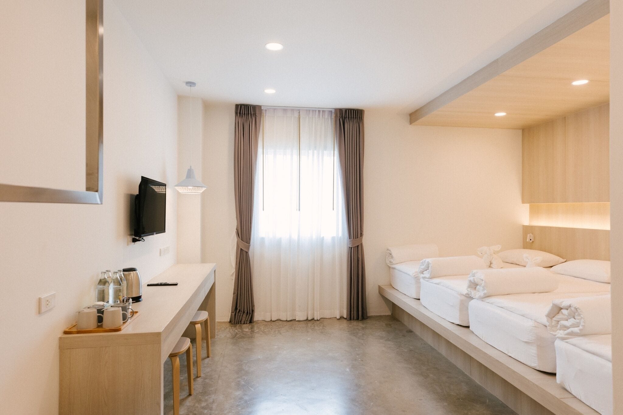 A hotel room with a desk, chairs, a TV, a window with curtains, and a bed with towels.