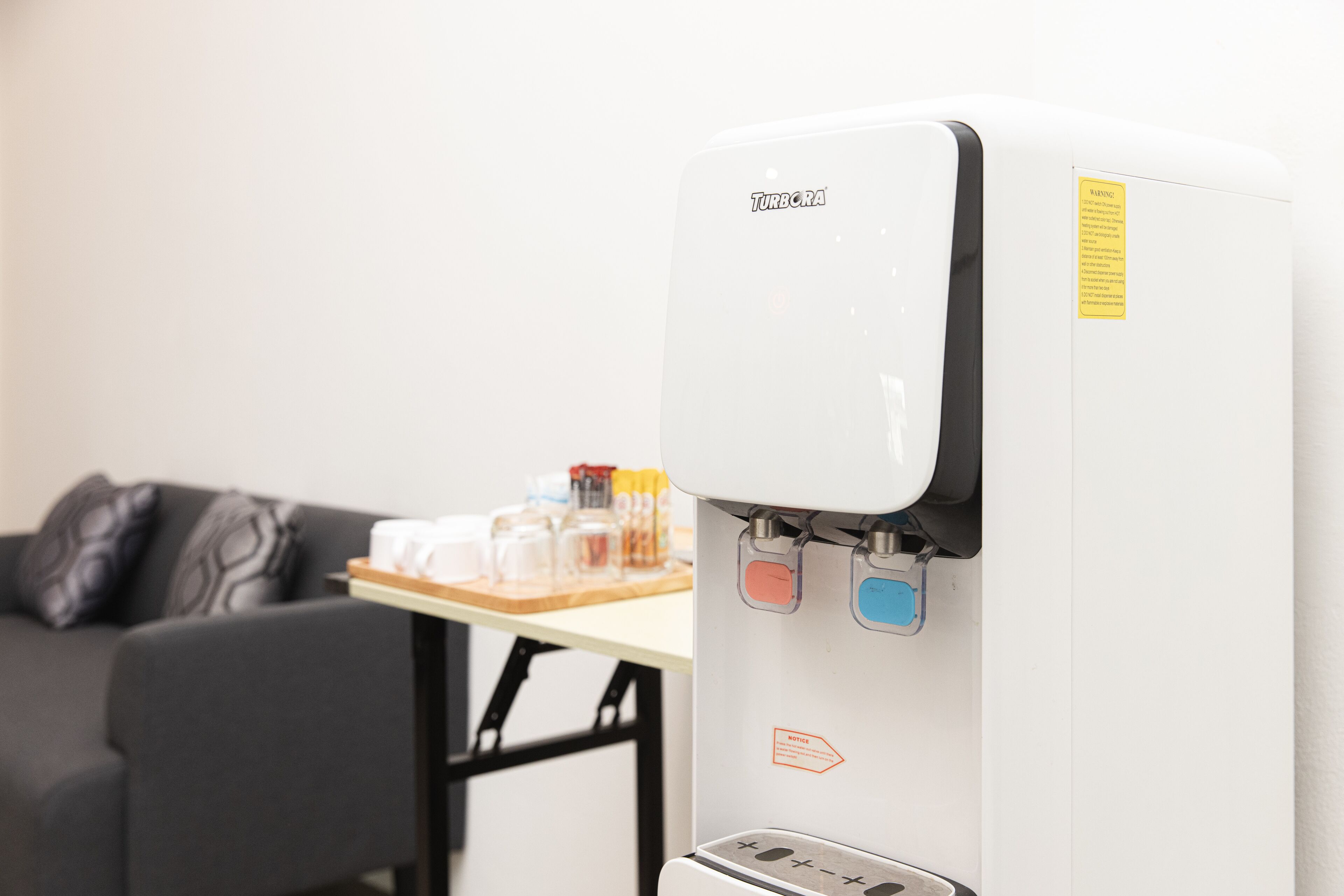 A water dispenser with a control panel and a table with various items in the background.