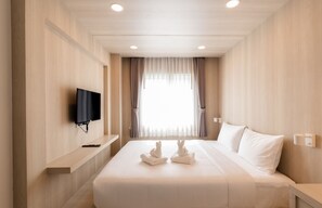Habitación de hotel con una cama grande, un televisor de pantalla plana montado en la pared, una mesita de noche y una ventana con cortinas.