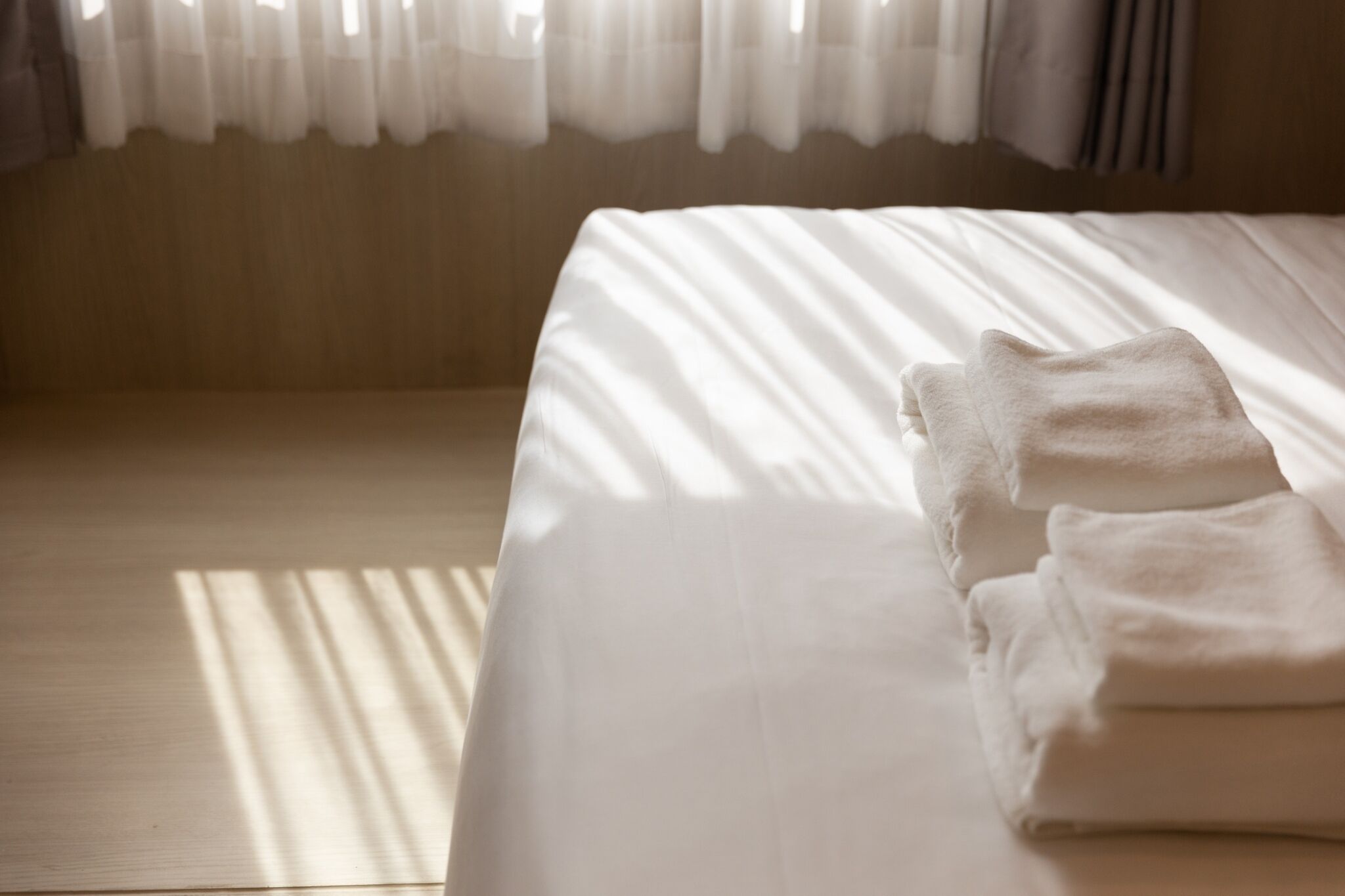 A neatly made bed with white linens and a folded towel on the right side.