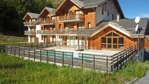 A chalet-style hotel with multiple balconies, a swimming pool, and a mountainous backdrop. - Luxurious Ski-In/Out Apartment with Pool, Sauna & Hammam - Sleeps 4, Free WiFi, Linens Included (Les Orres)