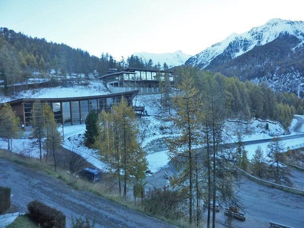 A modern building with large glass windows, surrounded by snow-covered mountains and trees.