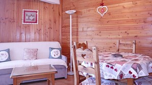 A cozy room with a wooden wall, a white sofa with patterned cushions, a wooden table, and a bed with a quilt.