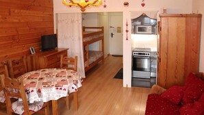 A cozy room with a bunk bed, a dining table with chairs, a red sofa, a wooden cabinet, and a kitchenette with a microwave and oven.