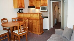 A compact kitchen with wooden cabinets, a dining table with chairs, a microwave, and a refrigerator.